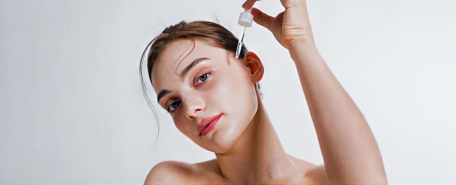 A woman applying serum with a dropper to her face for skincare routine.